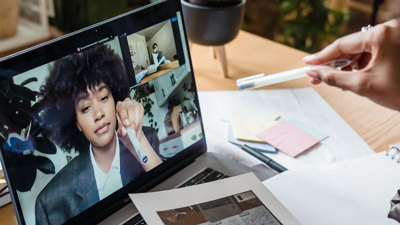 A laptop open to a video call, with documents beside it on the desk.